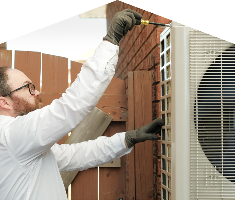 Furnace Guys service personnel working on an AC condenser, using a screwdriver to secure the unit’s panel outdoors beside a wooden fence. Furnace Guys service personnel working on an AC condenser, using a screwdriver to secure the unit's panel outdoors beside a wooden fence.