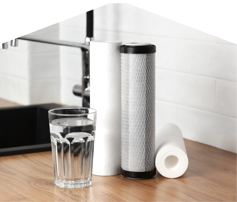 Set of Furnace Guys water filtration cartridges placed beside a clear glass of water on a kitchen countertop, with a sink and modern faucet in the background. Set of Furnace Guys water filtration cartridges placed beside a clear glass of water on a kitchen countertop, with a sink and modern faucet in the background.