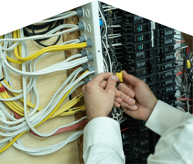 Furnace Guys service personnel working on electrical installations, connecting wires inside a residential breaker panel with neatly arranged colored cables on a plywood backing. Furnace Guys service personnel working on electrical installations, connecting wires inside a residential breaker panel with neatly arranged colored cables on a plywood backing.