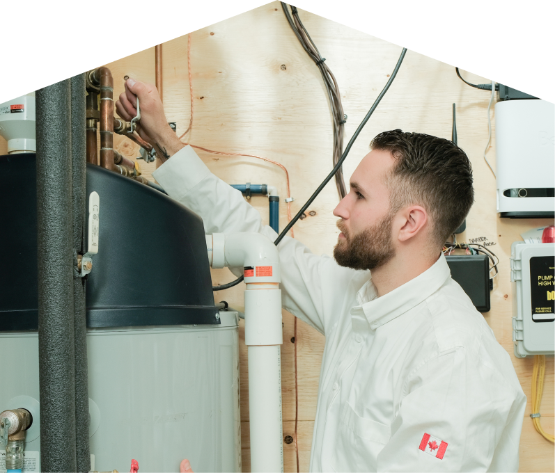 Furnace Guys water heater specialist adjusts piping on a large residential unit during a repair service, with exposed wood paneling and mounted utility components in the background.
